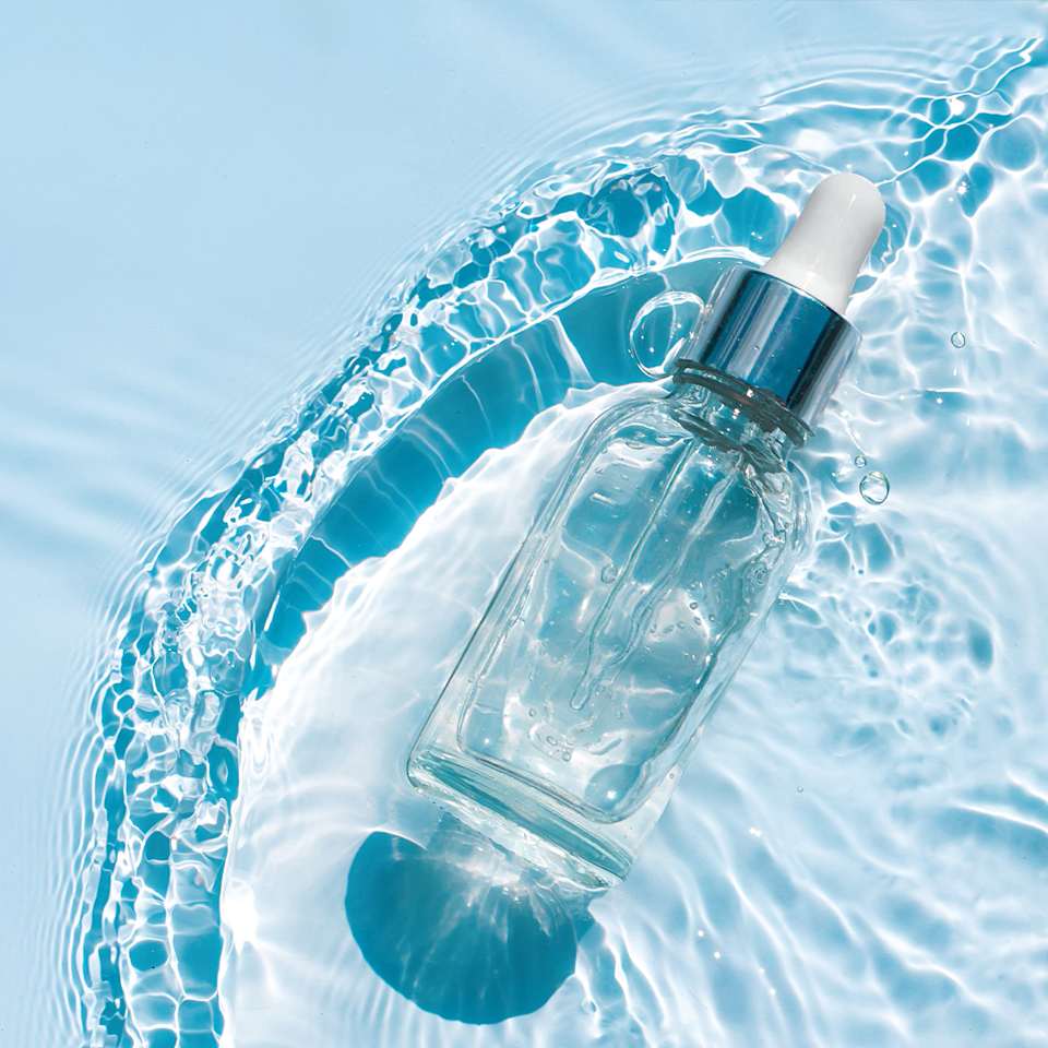 Serum-Flasche auf einem wasserbettähnlichen Untergrund vor blauem Hintergrund.