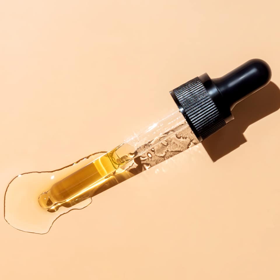 Retinol-Serum tropft aus Pipette auf hellorangem Hintergrund.