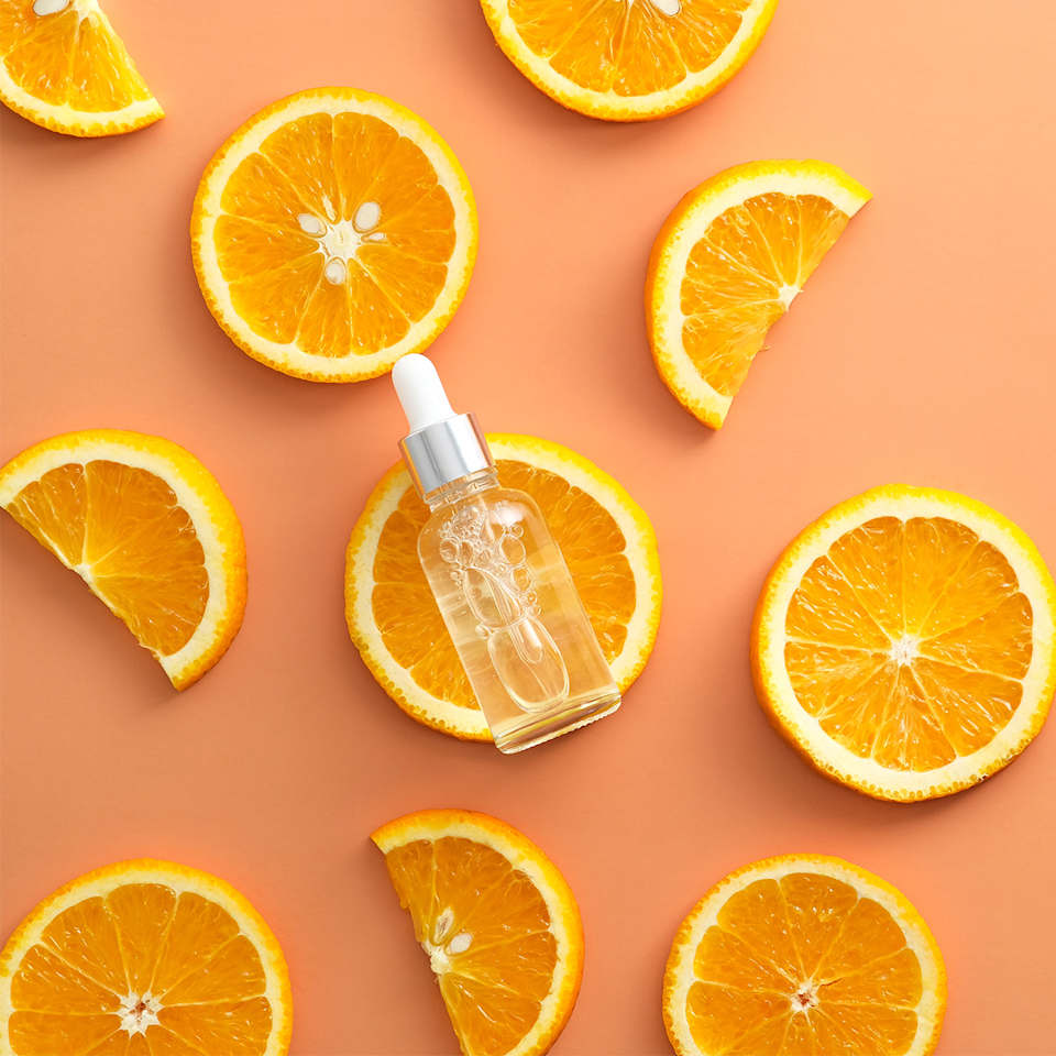 Vitamin-C-Serum für die Hautpflege zwischen Orangenscheiben auf orangefarbenem Hintergrund