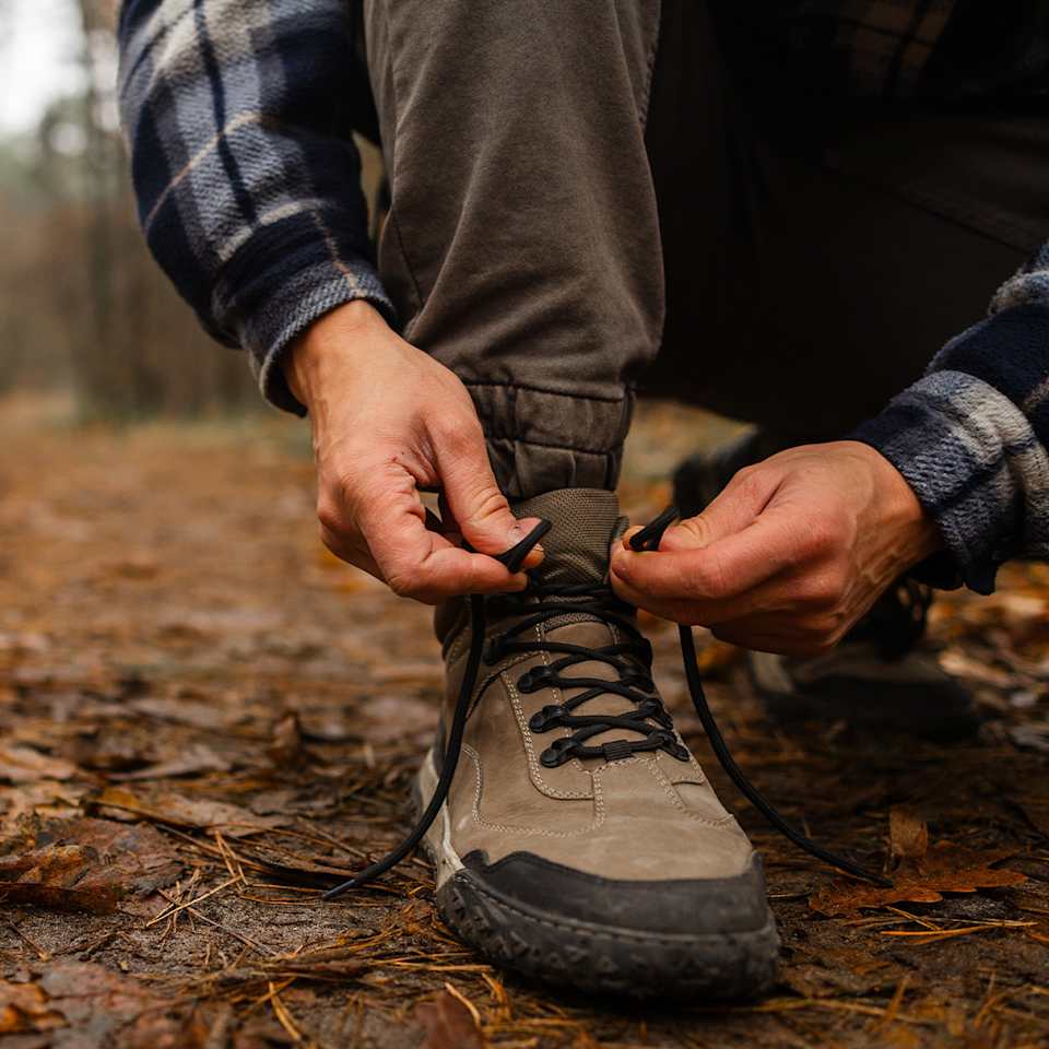 Mann kniet auf einen Waldboden der mit buntem Laub bedeckt ist und bindet sich seine Wanderschuhe.