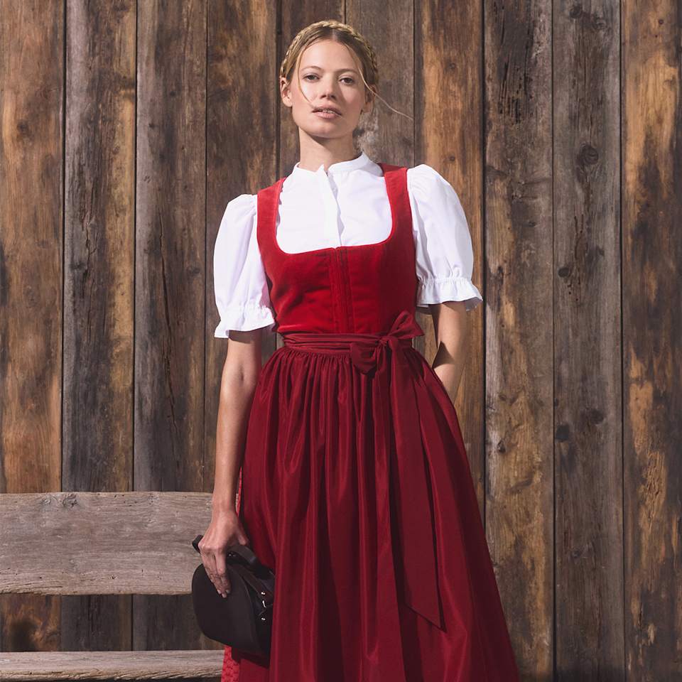 Blonde Frau trägt rotes Dirndl mit Schleife