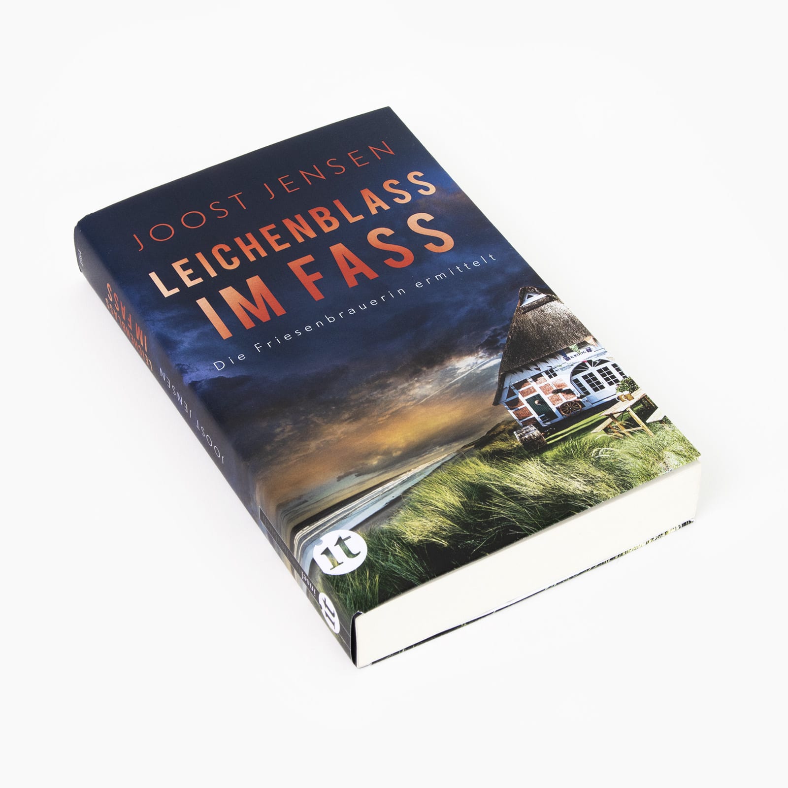 Das Buch »Leichenblass im Fass« des Autors Joost Jensen liegt auf weißem Hintergrund. Das Cover zeigt ein Fachwerkhaus am Meer in stürmisch-düsterer Stimmung.