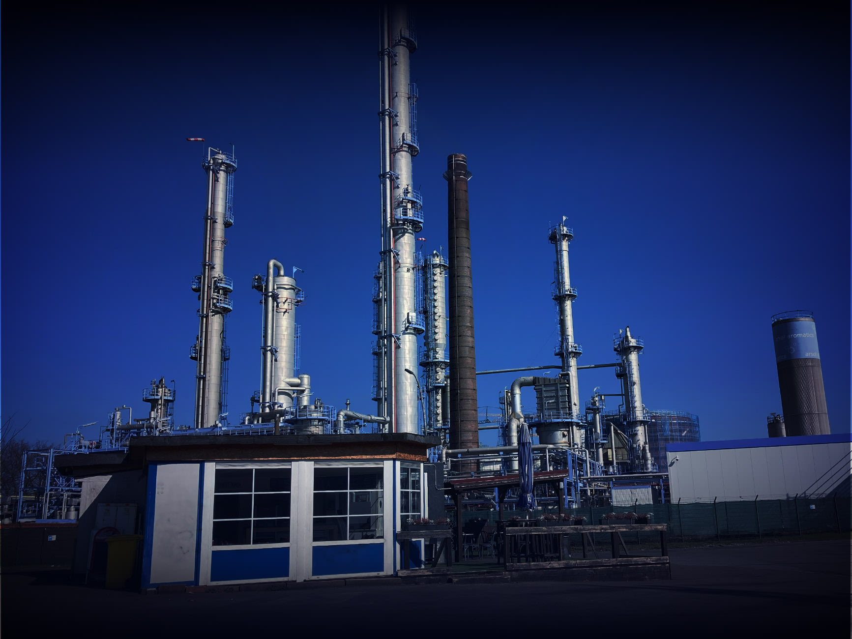 Blick auf blau-weiße Imbissbude mit Industriekaminen im Hintergrund 