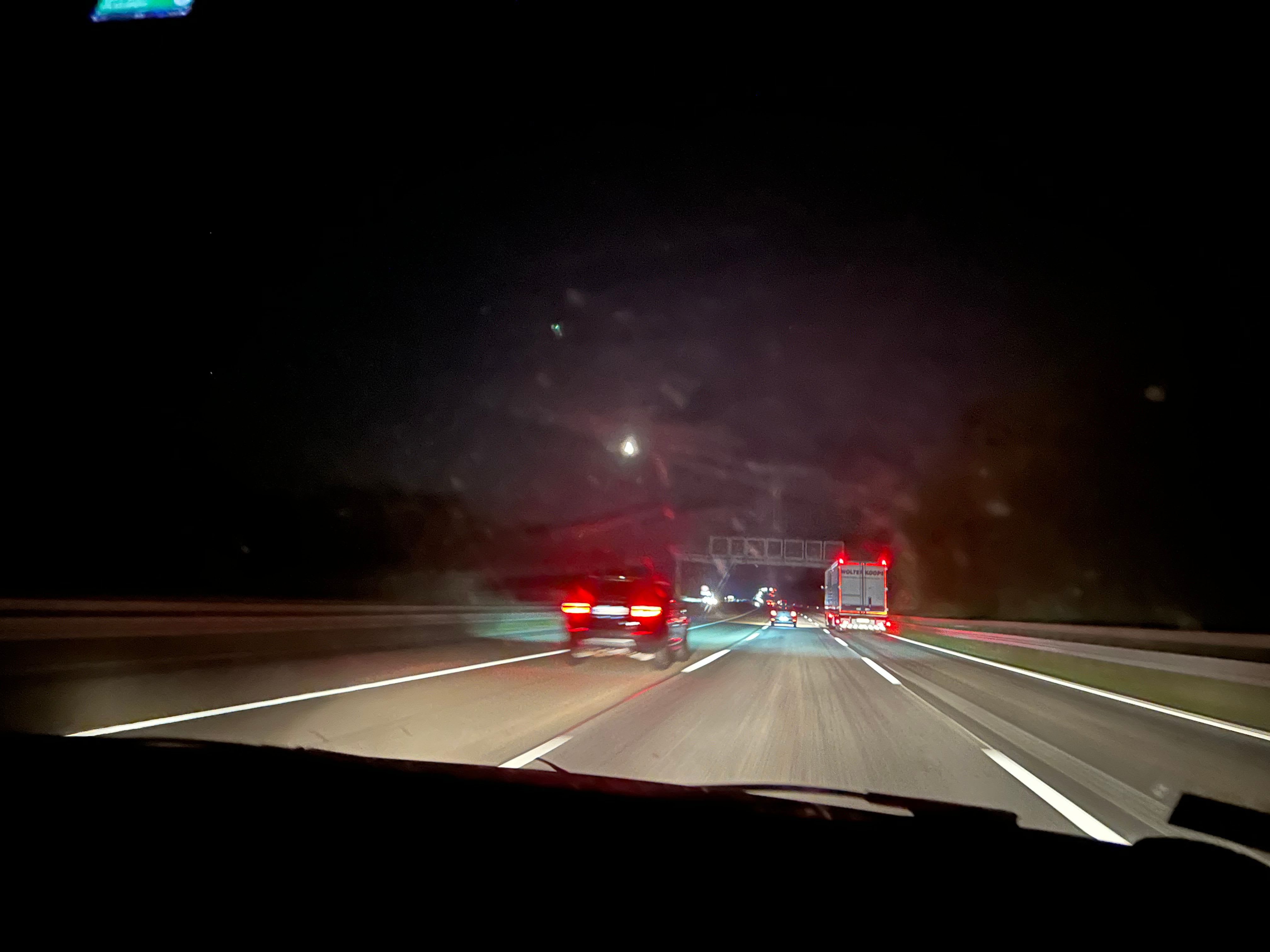 Eine Autobahn bei Nacht. Das Foto wurde während des Fahrens vom Beifahrersitz aus durch die Windschutzscheibe aufgenommen und zeigt vorneweg fahrende Autos auf der Autobahn. Copyright: Yannic Han Biao Federer
