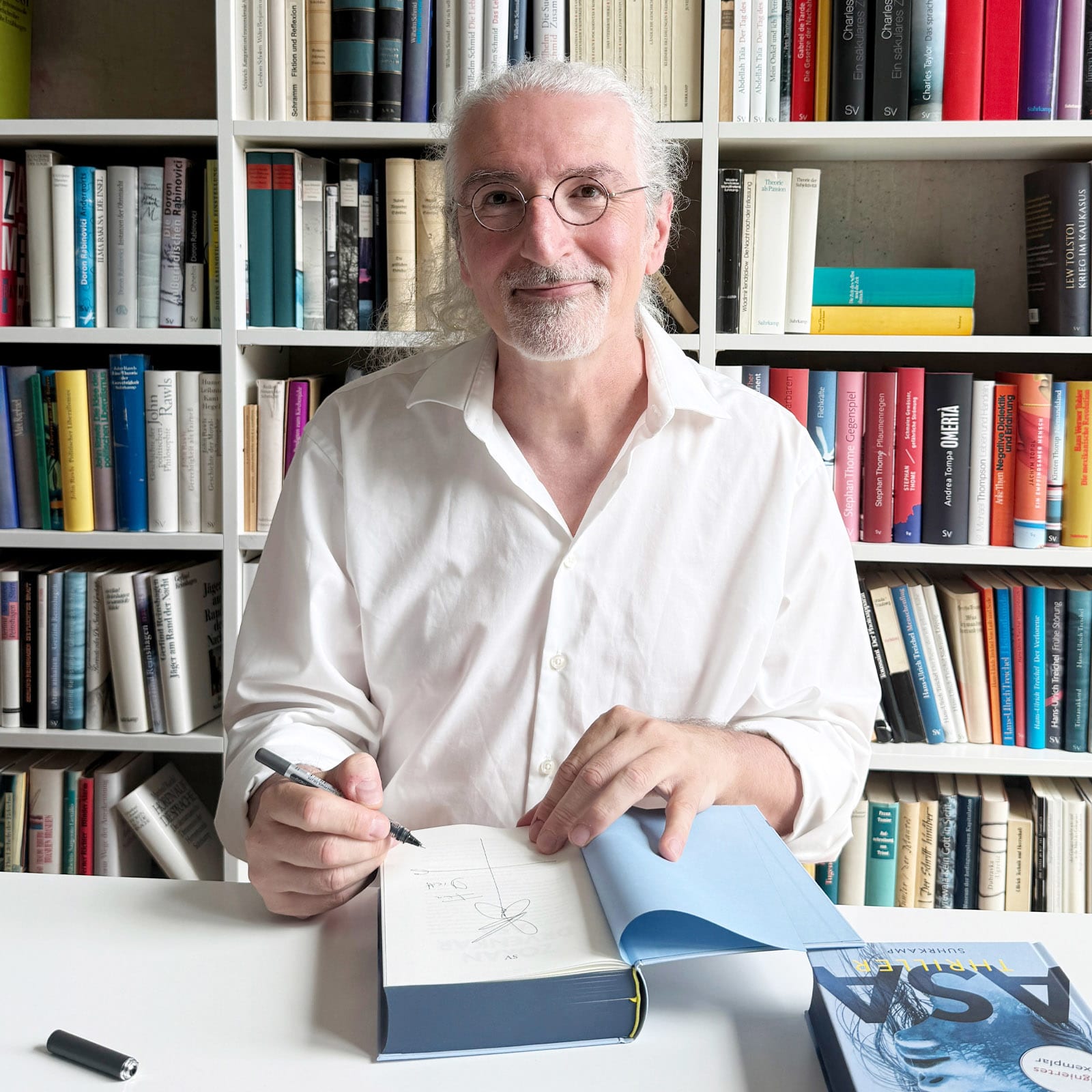 Zoran Drvenkar guckt in die Kamera und signiert eines seiner Bücher.