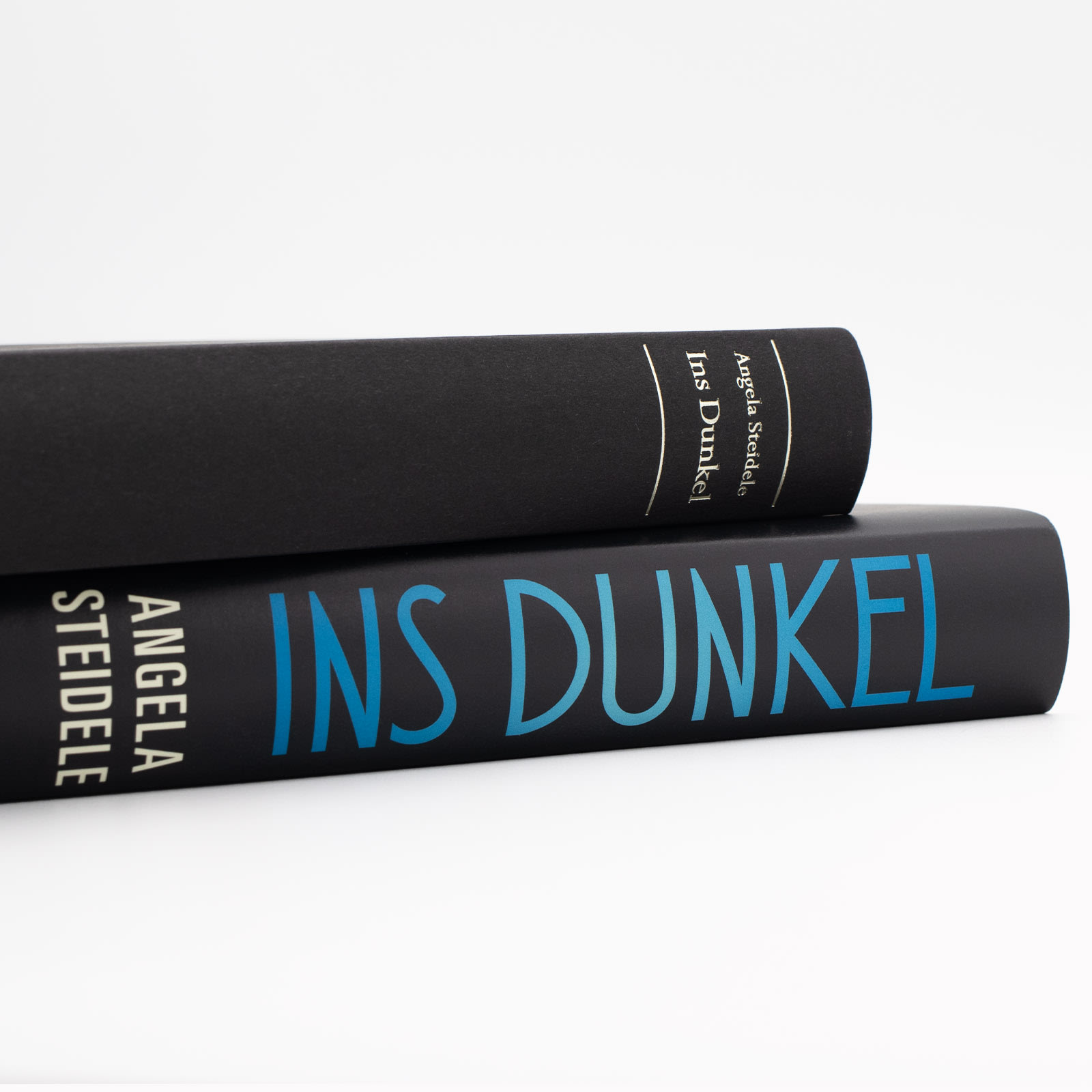 Der Buchrück von »Ins Dunkel« einmal mit Schutzumschlag, und einmal ohne