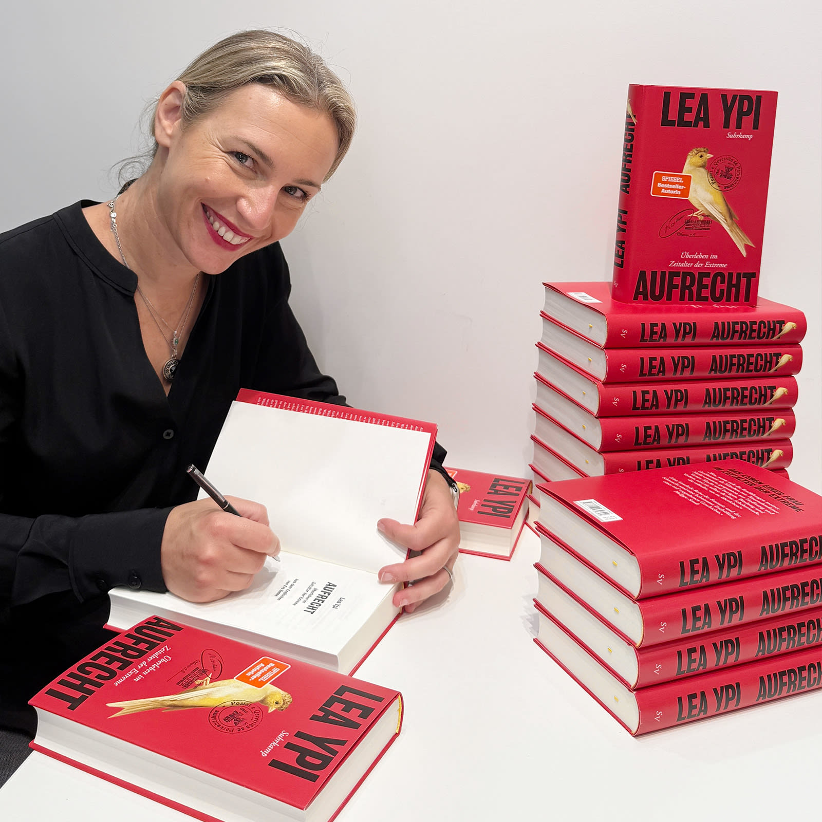 Ein Foto von Lea Ypi beim Signieren, neben ihr befindet sich ein Stapel ihrer Bücher.