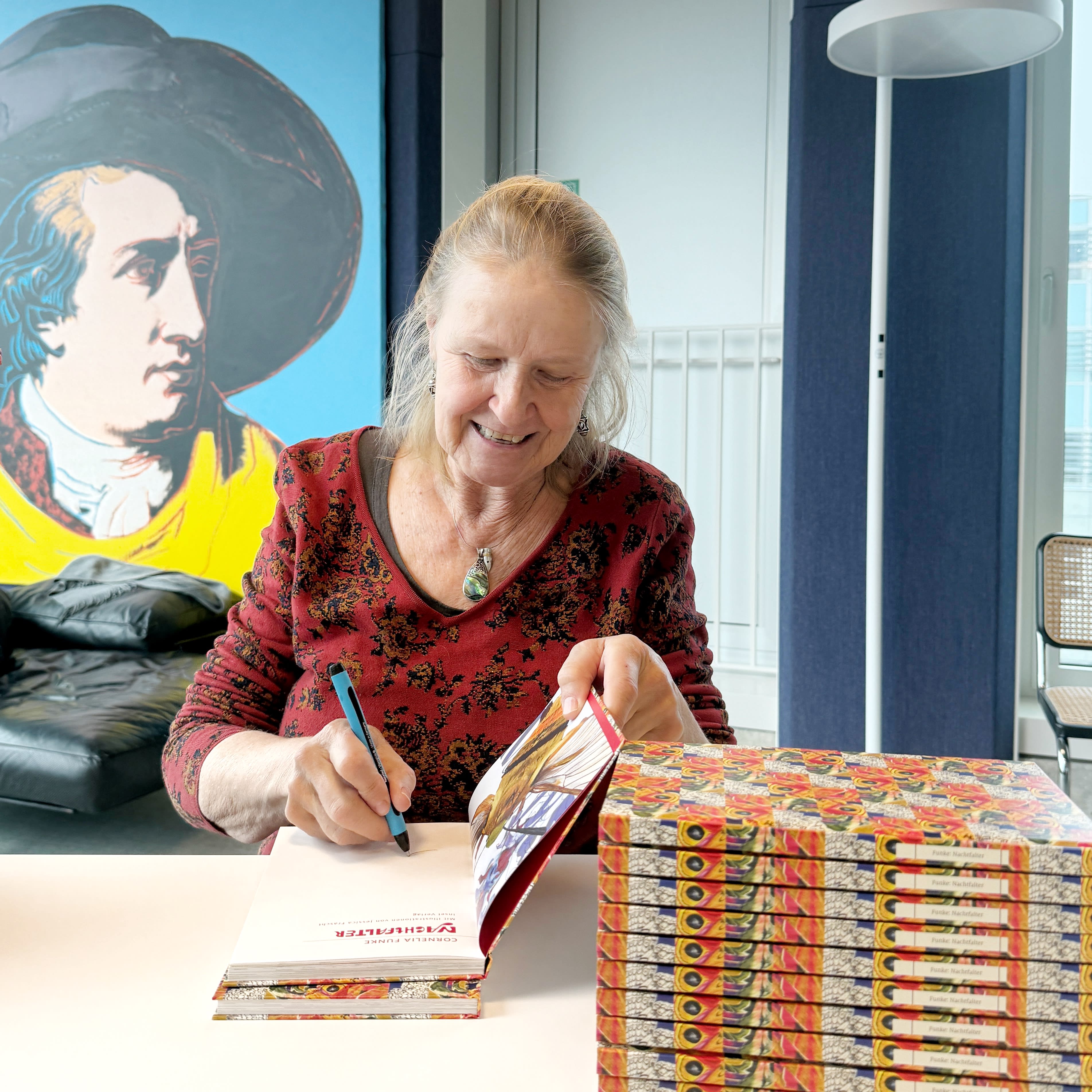 Ein Foto von Cornelia Funke beim Signieren mit Blick zum aufgeschlagenen Buch