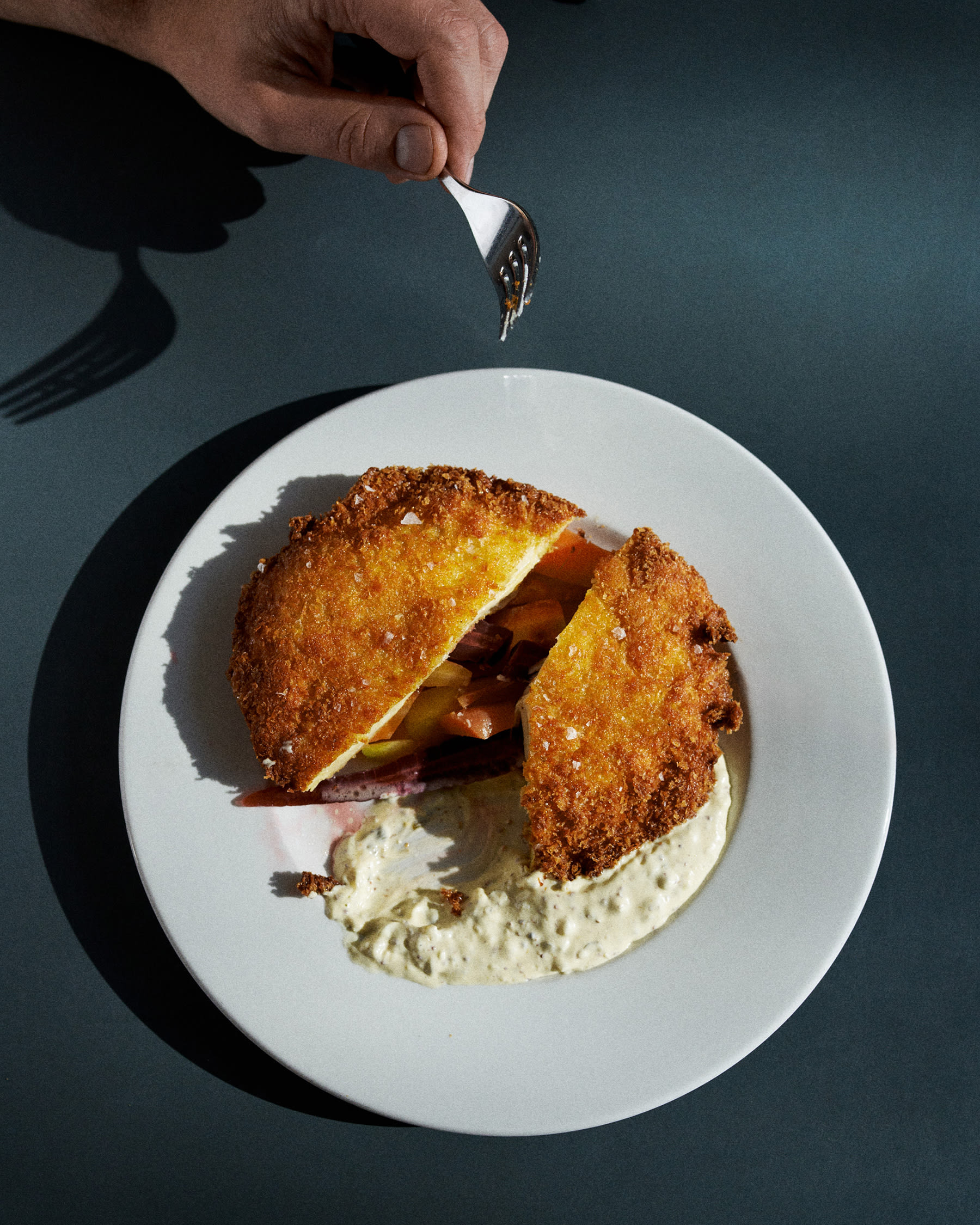 Gebackenes Sellerieschnitzel in Soße auf weißem Teller und grauem Untergrund