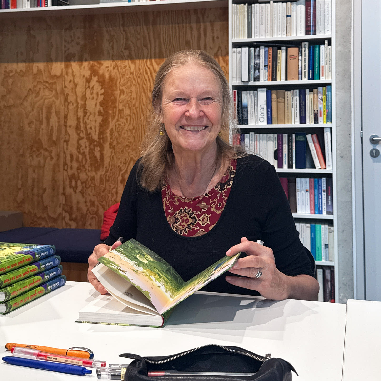Ein Foto von Cornelia Funke beim Signieren, neben ihr befindet sich ein Stapel ihrer Bücher.