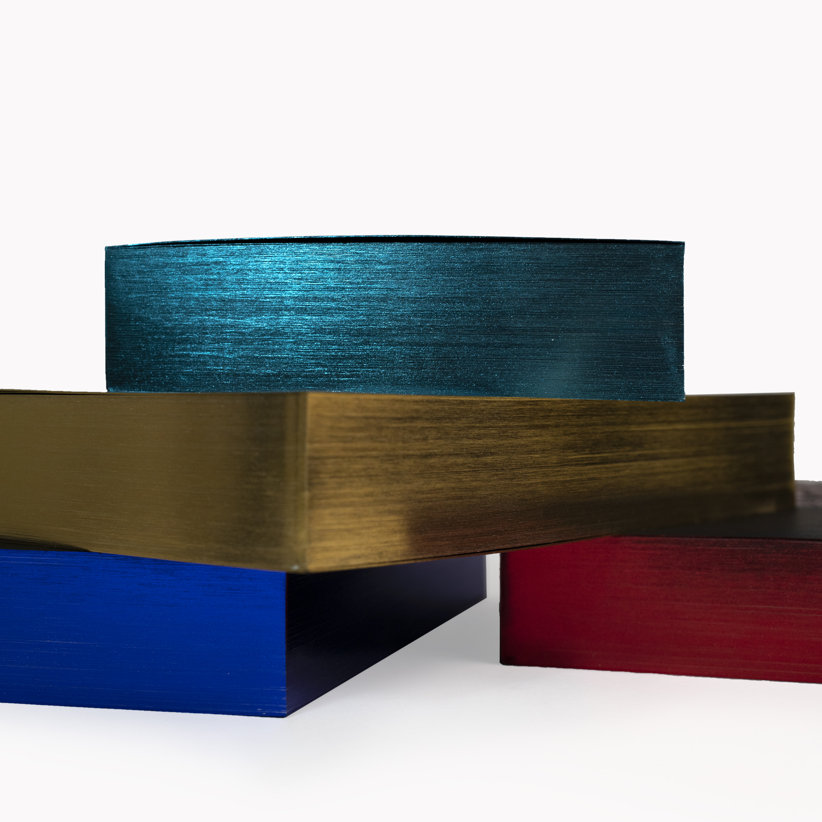 Ein Stapel mit vier Ausgaben des Buches »Ulysses« von James Joyce mit jeweils verschiedenfarbiger Prägung. Die Ausgaben sind von der Seite fotografiert, zu sehen sind die Bände in den Farben Türkis, Blau, Gold und Rot.