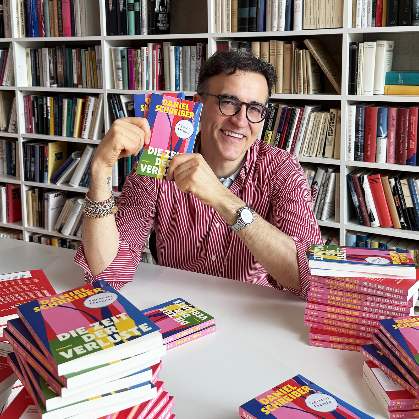 Daniel Schreiber vor einer Bücherwand mit Blick in die Kamera und Buch in der Hand