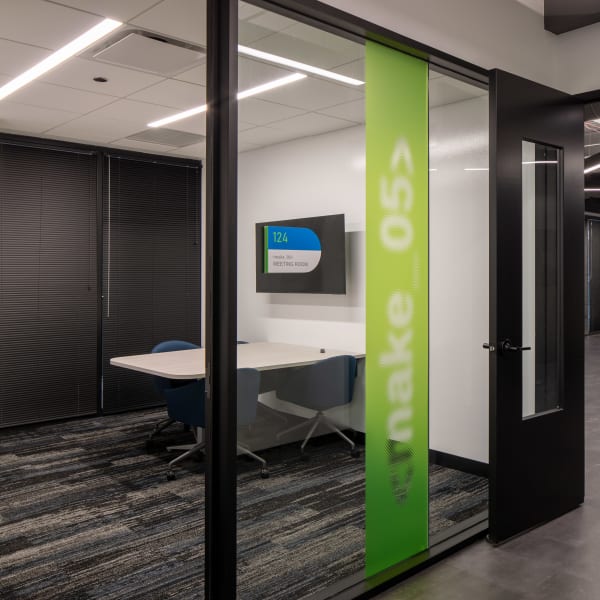 Wayfinding signage showing room number 124 and Meeting Room label on wall-mounted plaque with green decorative film.