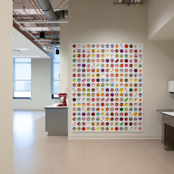 Large white wall panel with routed circular pockets displaying individual candy samples in colorful grid.