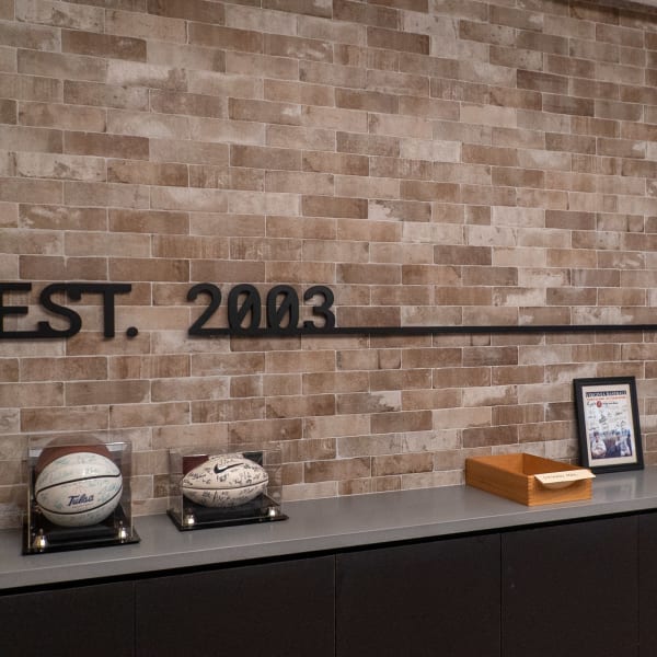 Black dimensional lettering reading EST. 2003 mounted on an exposed brick wall above storage cabinets.