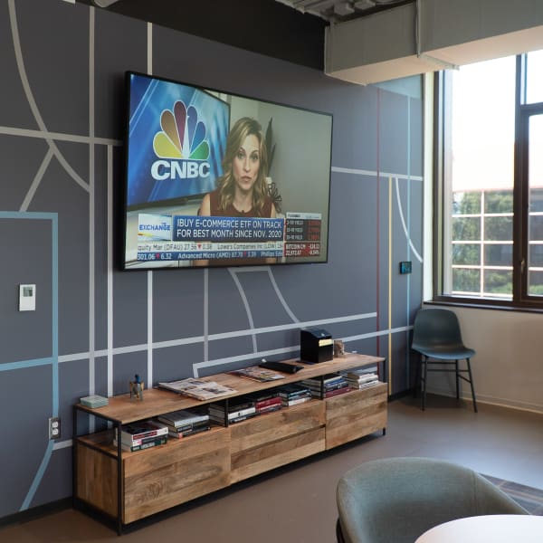 Office break room featuring environmental branding with curved line street-map graphics on gray walls behind mounted television.