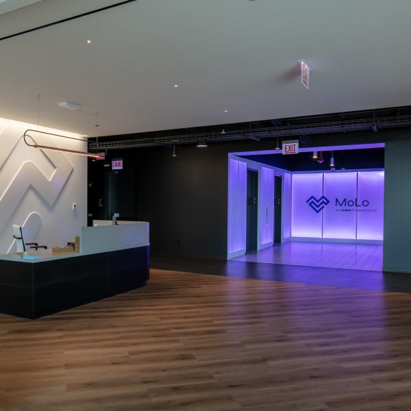 Office lobby features reception desk with backlit geometric logo on white wall.