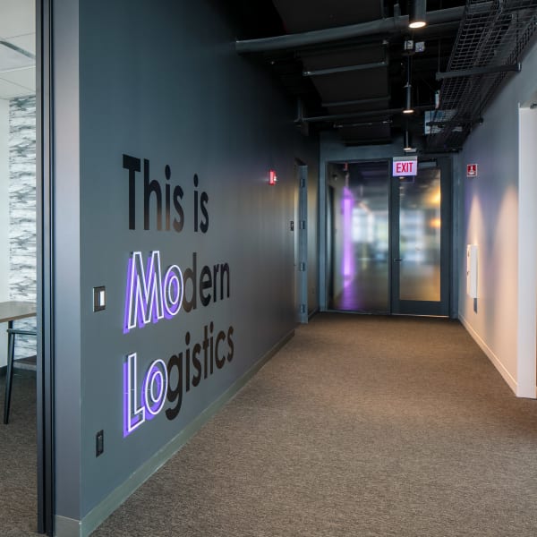 Office wall graphics with purple LED-lit letters in hallway near glass-walled conference room.