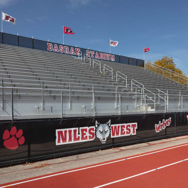 Environmental branding features Niles West text, wolf mascot, and paw graphics on black fence along running track.