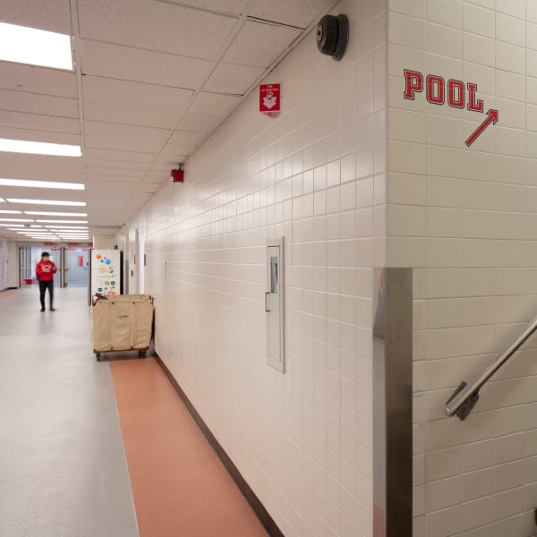 Navigational signage on white tile wall reads Pool with arrow pointing right in red lettering.