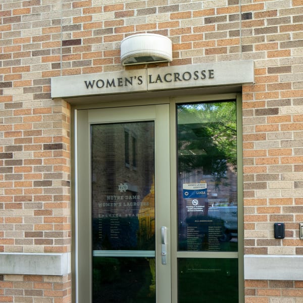Women's Lacrosse entrance door with window graphics displaying team roster and schedule on glass panels.