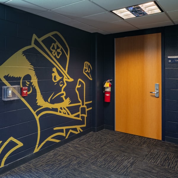 Office wall graphics featuring large gold Notre Dame Fighting Irish leprechaun mascot on navy painted cinder block.