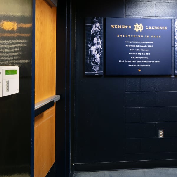 Office wall graphics displaying Women's ND Lacrosse heading and 'Everything is Odds' motto with player silhouettes.