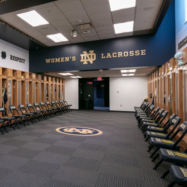 Locker room logo featuring Women's ND Lacrosse dimensional lettering in gold on navy wall with floor logo.