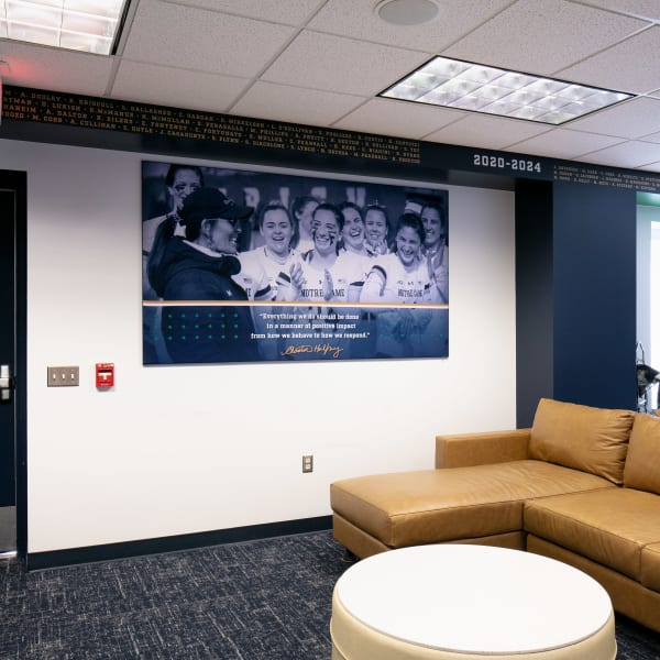 Office wall graphics with framed team celebration photo mounted on navy painted wall above tan leather sectional.