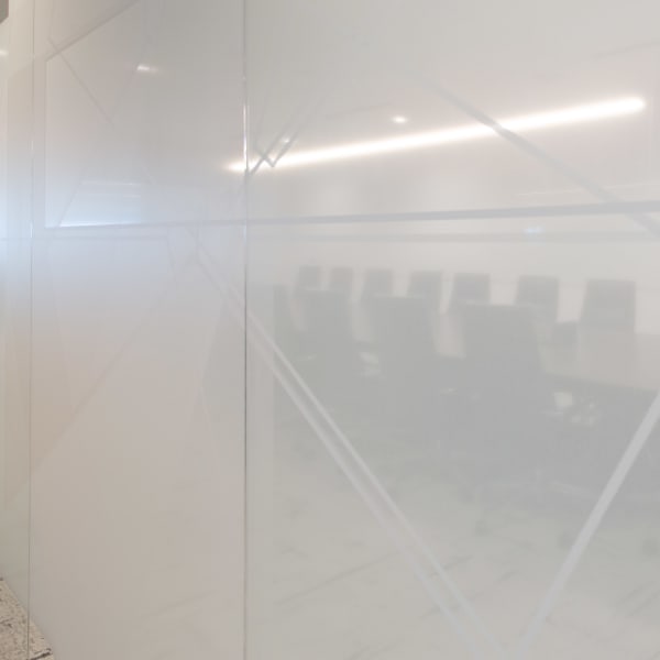 Office window frosting displaying translucent geometric logo pattern etched into meeting room glass.