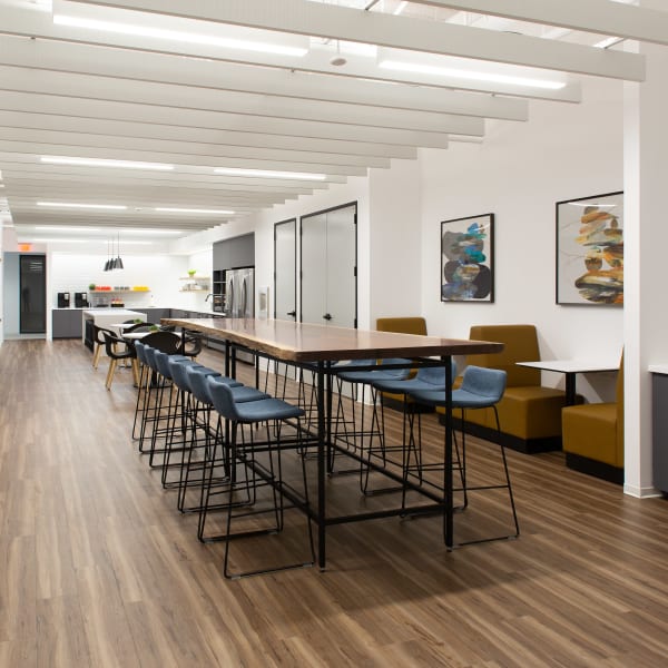 Modern office breakroom with high-top seating, pendant lighting, and open kitchen area.