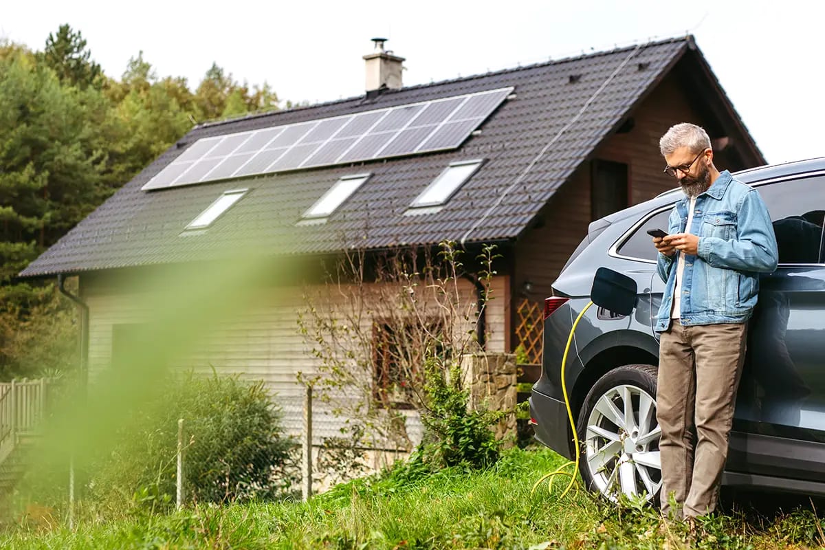 Mann lädt E-Auto vor Haus mit Photovoltaik