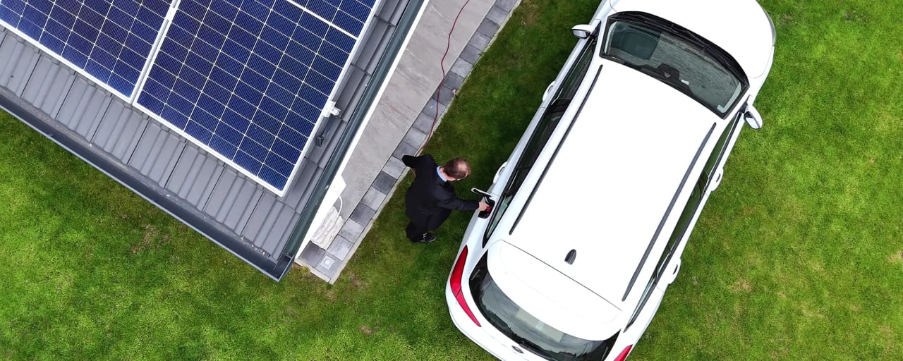 Luftaufnahme E-Auto an Wallbox neben Haus mit PV