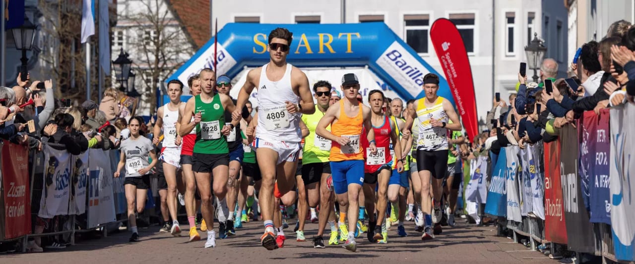 Läufer starten bei einem Stadtlauf, angefeuert von jubelnden Zuschauern entlang der Strecke.