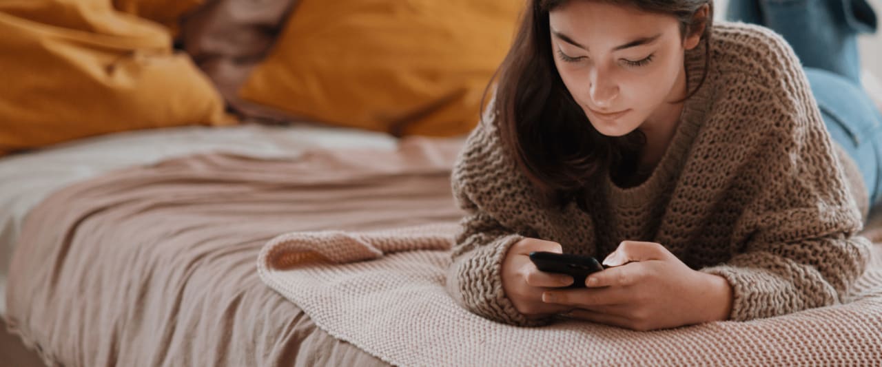 Junge Frau auf dem Bett mit einem Handy in der Hand.