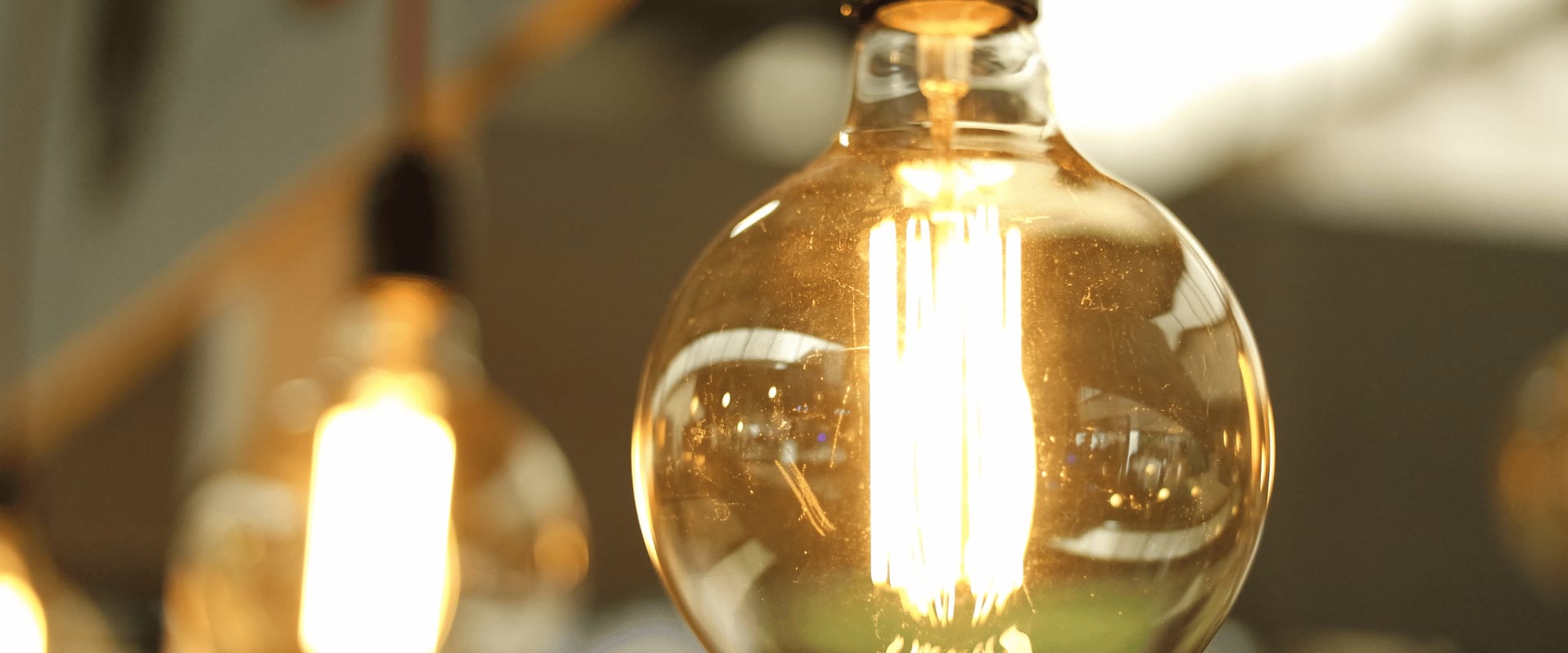 Nahaufnahme einer leuchtenden Glühbirne im Vintage-Stil, mit warmem Licht in einem unscharfen Innenraumhintergrund.