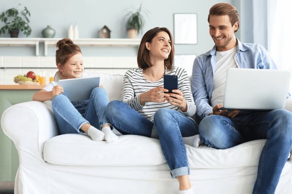 Junge Familie mt einem Kind sitzt auf dem Sofa mit Laptops und einem Handy.