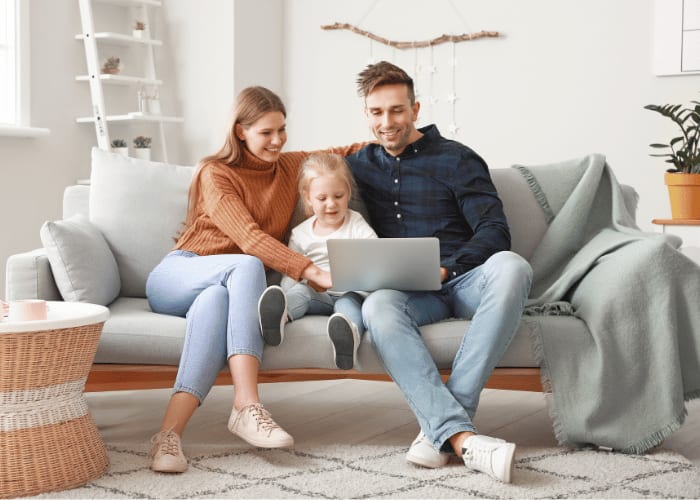 Familie sitzt gemeinsam auf dem Sofa und nutzt einen Laptop im Wohnzimmer.