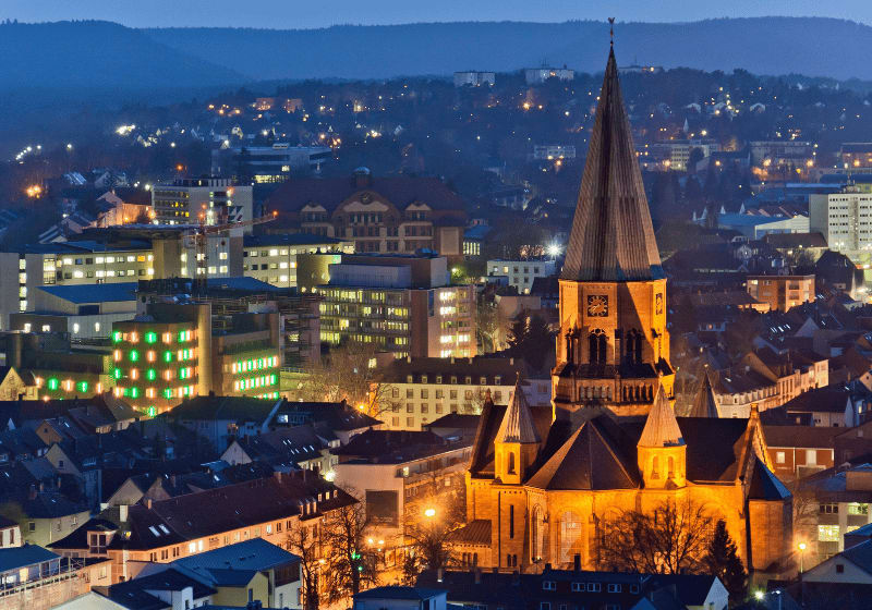 Die Stadt Kaiserslautern bei Nacht mit der beleuchteten Apostelkirche im Vordergrund.