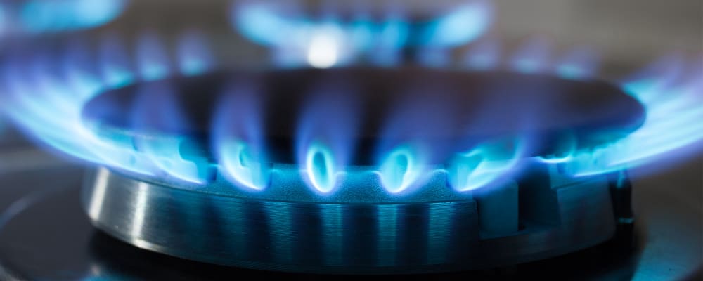 Nahaufnahme eines Gasherds mit blauer Flamme – die Brennerflammen kreisen gleichmäßig um den Metallaufsatz.