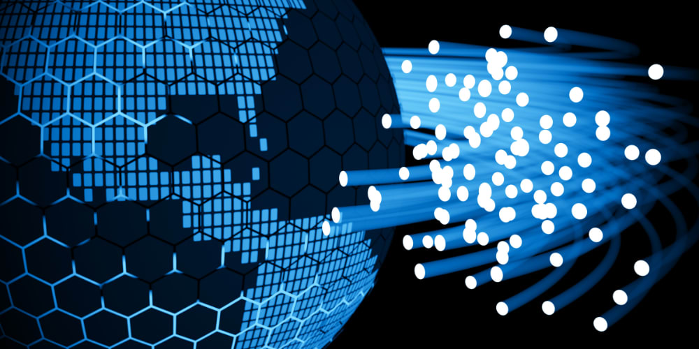 Digitale Darstellung eines Globus mit hexagonalem Muster in Blautönen. Von der rechten Seite verlaufen leuchtende, blaue Lichtstrahlen mit vielen Lichtpunkten in Richtung der Erdkugel, symbolisierend für Glasfasertechnik, Datenübertragung oder weltweite digitale Vernetzung. Der Hintergrund ist schwarz, was den Kontrast der blauen Elemente verstärkt.