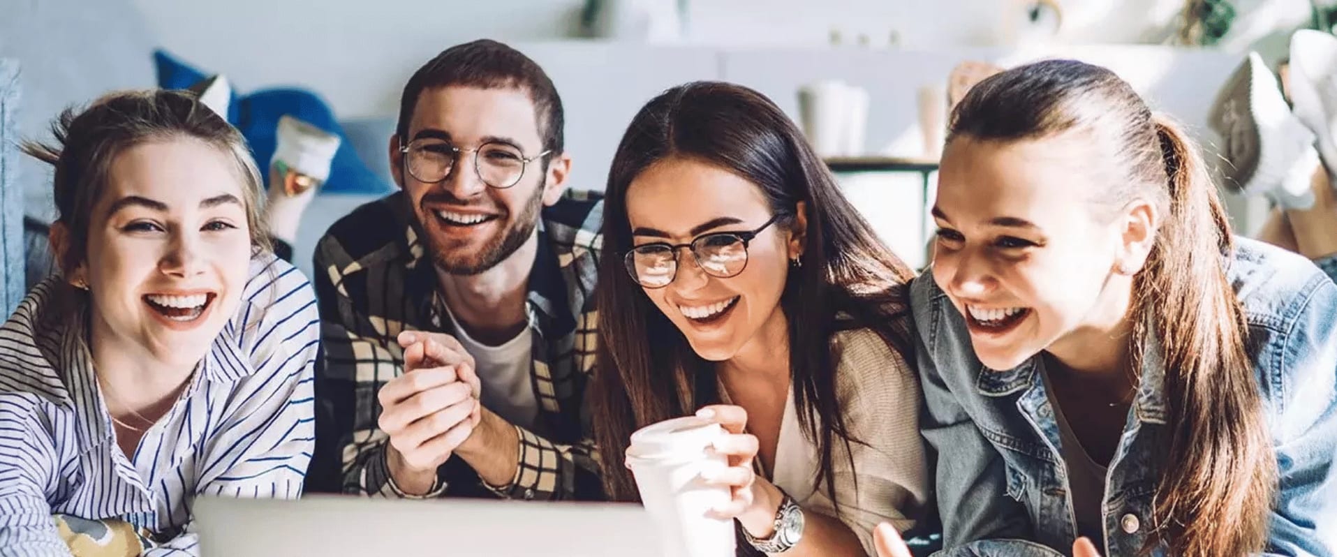 Vier junge Erwachsene sitzen lachend zusammen und schauen auf einen Laptop.