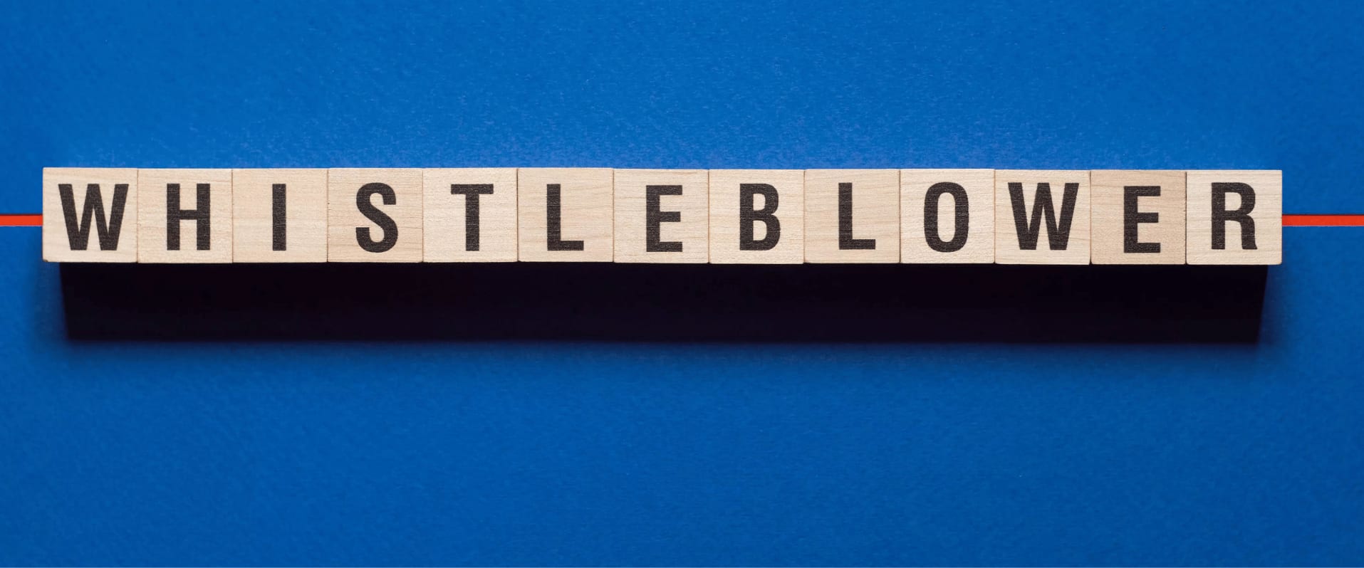 Holzbuchstabenwürfel bilden das Wort Whistleblower auf blauem Hintergrund.