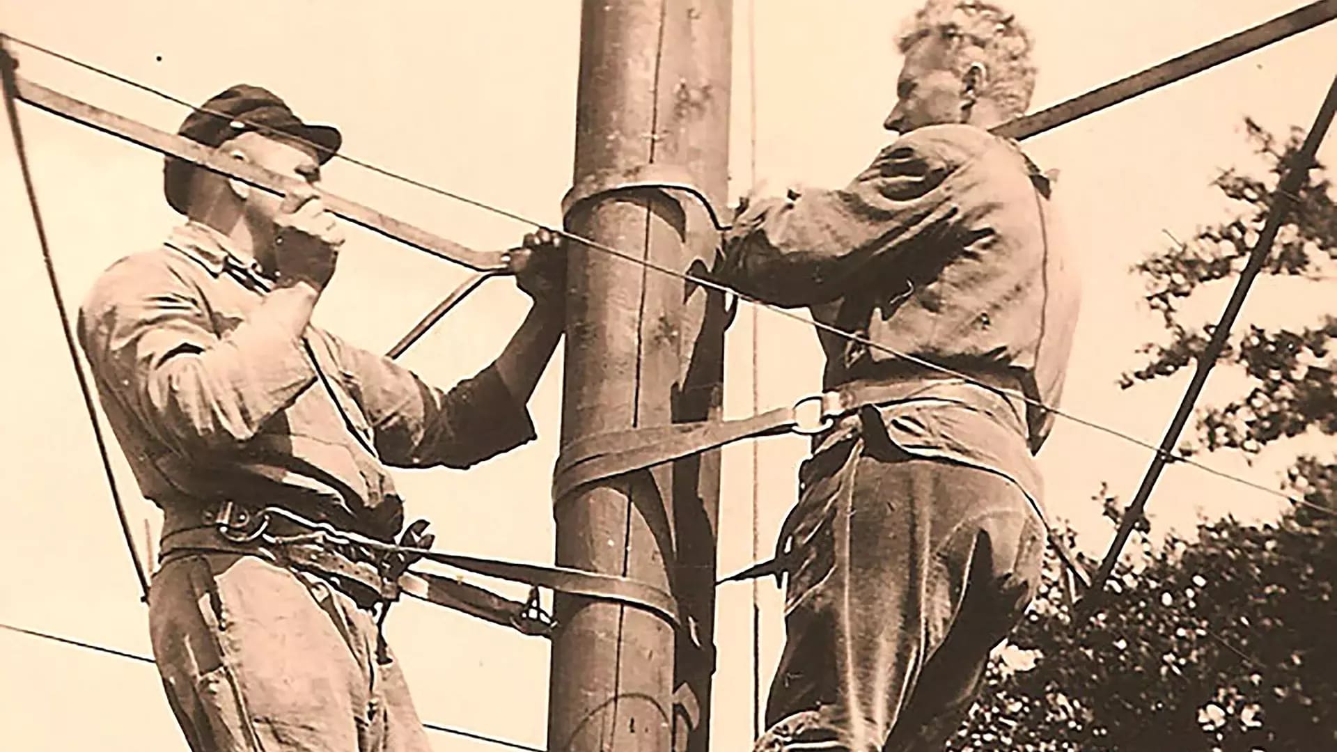 Zwei Monteure bei der Arbeit an einem Strommast in historischer Aufnahme.