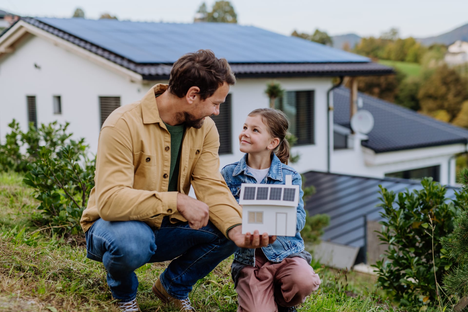 Familienvater mit Tochter hält ein Modellhaus mit PV in der Hand.