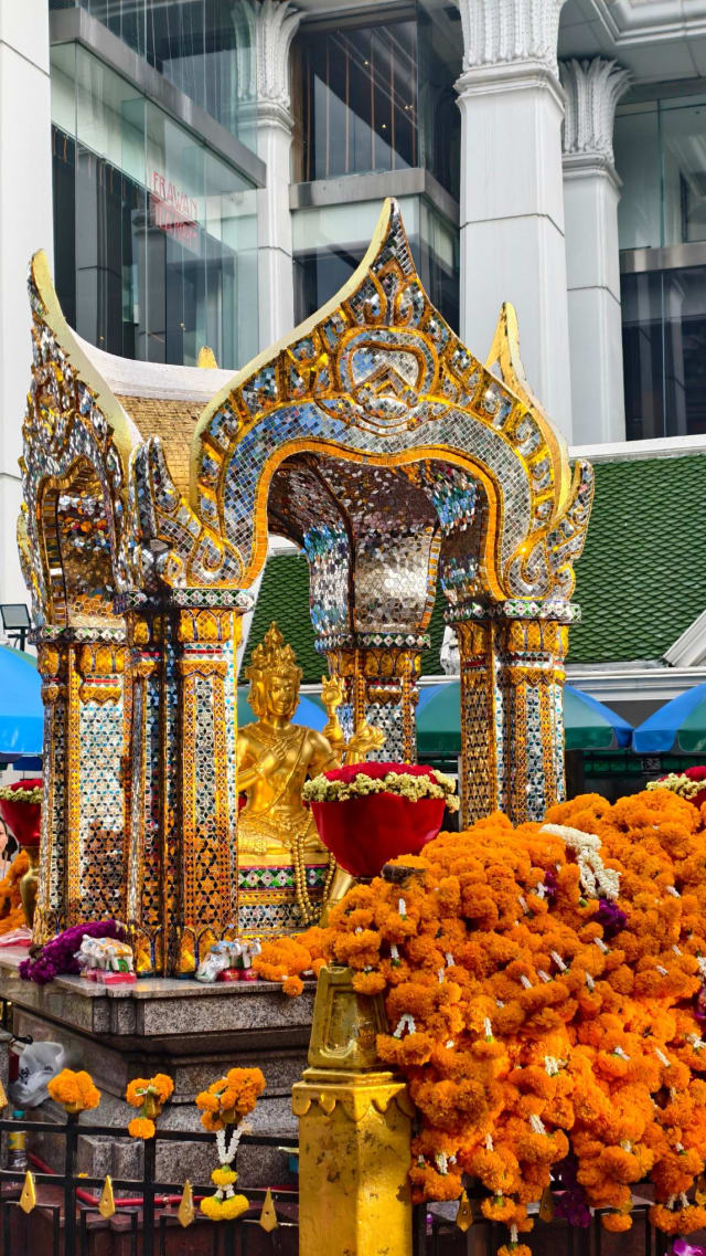 The shrine pavilion with marigold garland offerings in the foreground and modern glass buildings behind