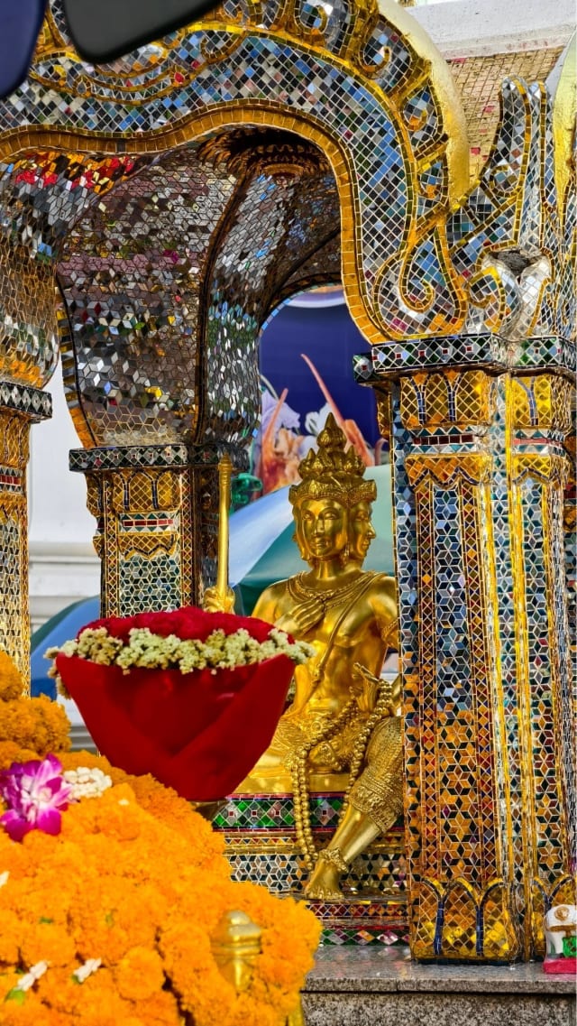 The Brahma image viewed through the mirrored glass archway of the pavilion, with a floral offering tray