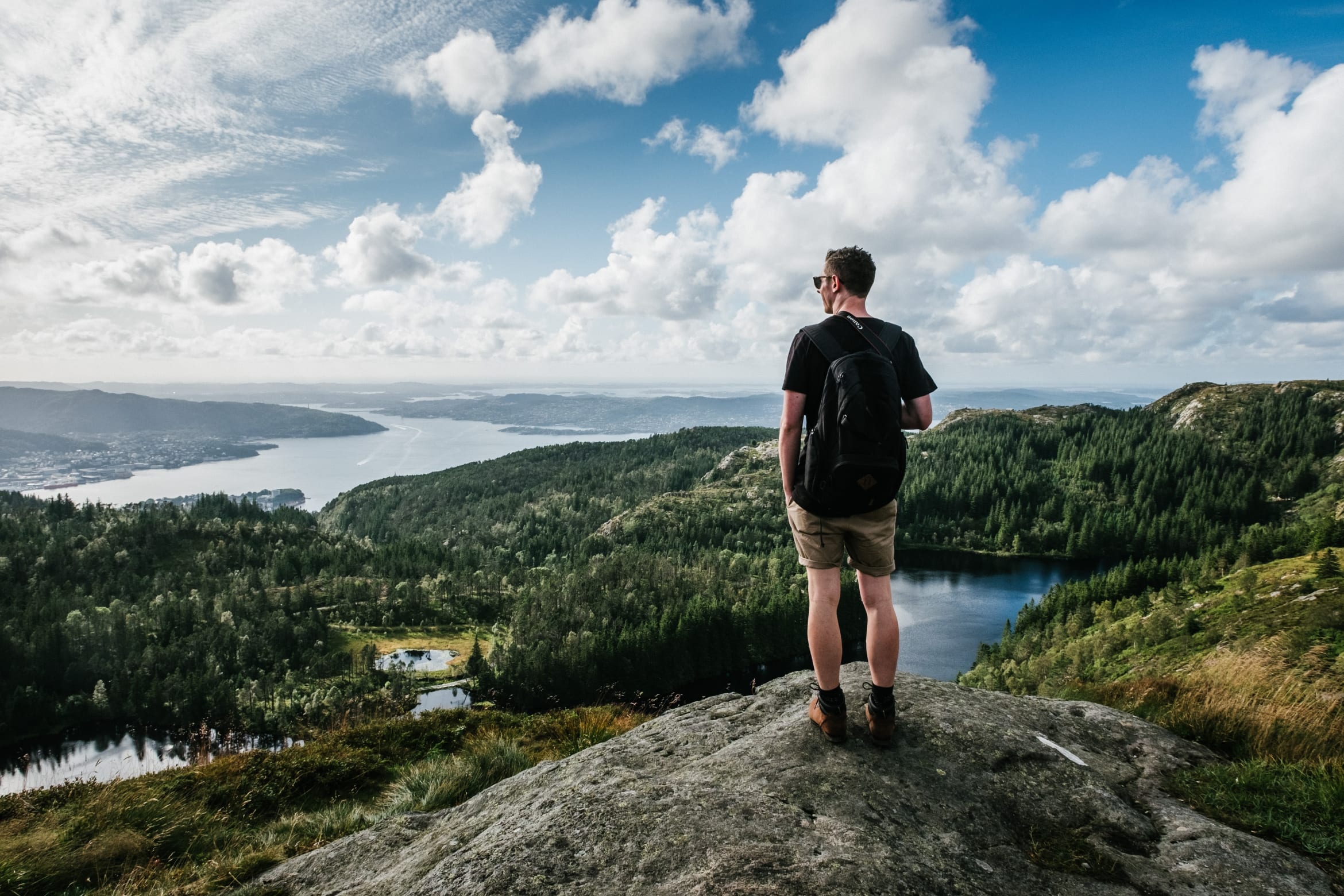 Young man standing on a rock overlooking a breathtaking view of trees and cloudy skies