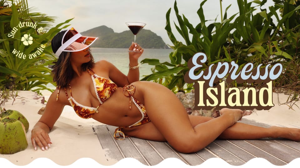 A model lounges on a sandy beach, wearing a vibrant orange tropical bikini and a white visor, holding a cocktail. Lush greenery and mountains frame the backdrop.