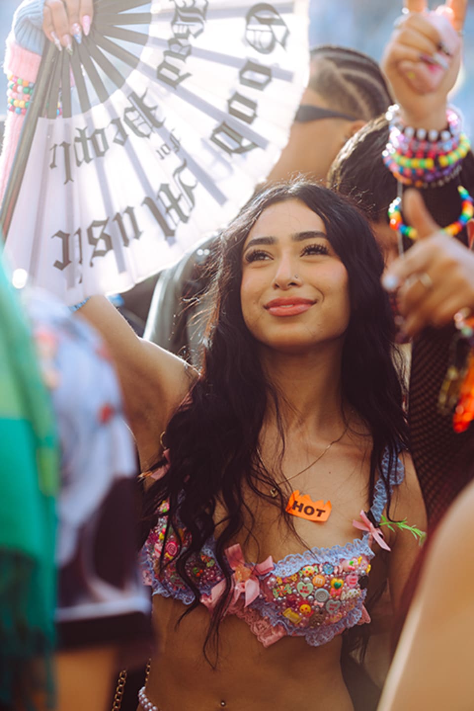 Stylish woman dancing at sunset during an outdoor music festival, surrounded by glowing lights and a vibrant crowd atmosphere.